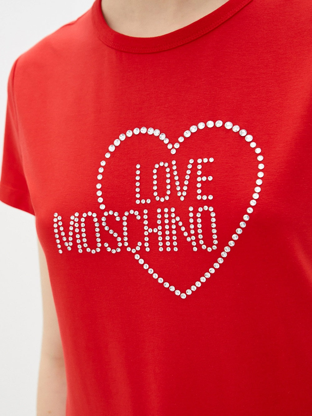 T-Shirt Love Moschino W4F731HE1951 realizzata interamente in cotone. Frontalmente la T-Shirt presenta dei brillantini applicati a formare il lettering del brand e cuore incorniciato.